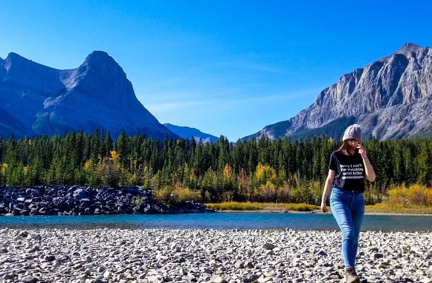 me walking on the rocky riverbank with mountains behind me