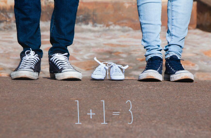 two adults legs from the knees down and a pair of baby shoes placed between them