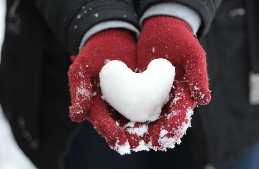 wearing winter gloves and holding snow in the shape of a heart. Gloves stop the dangers of hiking like frostbite