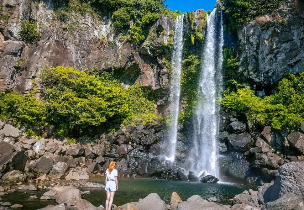 Me wearing white clothes standing in front of the Jeongbang waterfall in Seogwipo, Jeju