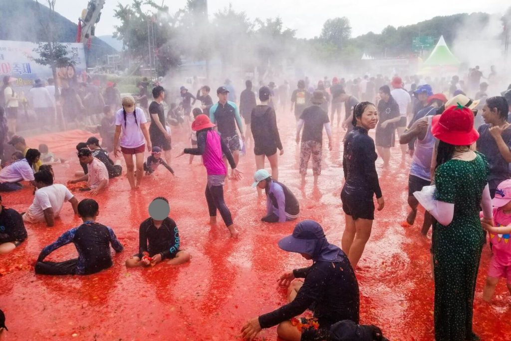 The steaming tomato pool with water hose raining from above and a crowd of people in the Hwacheon fest in Korea